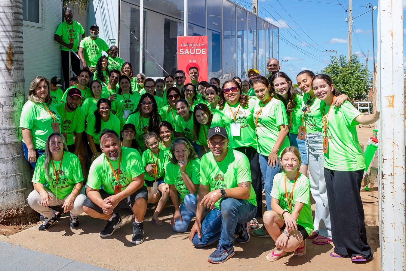 Grupo de voluntários de camiseta verde posando juntos em frente à Carreta da Saúde